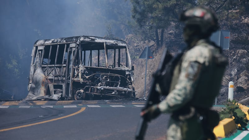 A soldier stands guard by a charred vehicle after it was set on fire, in Cointzio, Michoacán...